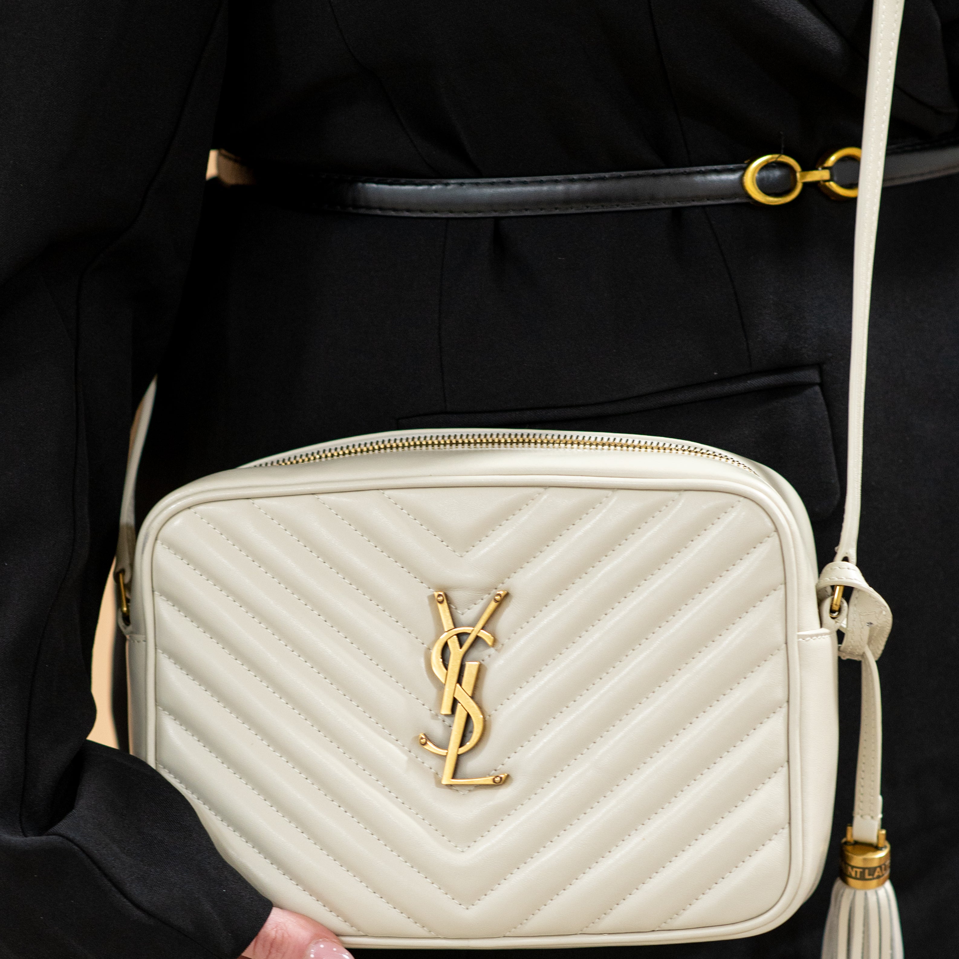 White quilted handbag with a gold ysl logo held by a person wearing a black coat.